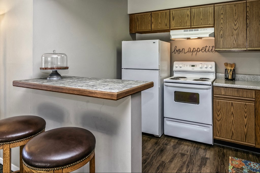 a kitchen with white appliances and a counter with two stools