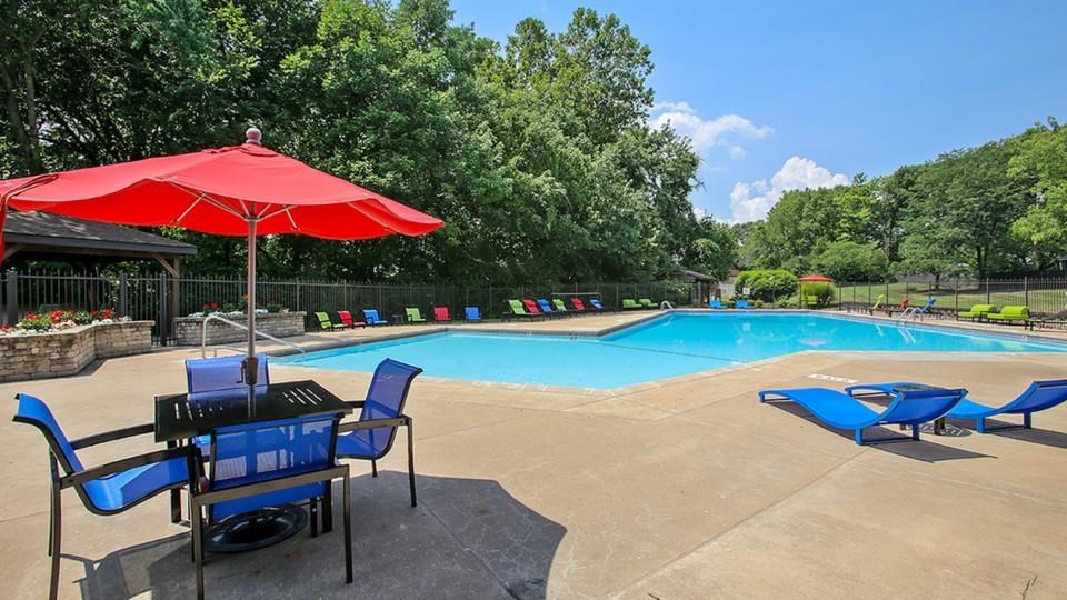 A pool area with a red umbrella and blue chairs.