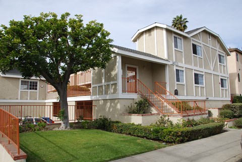 A tree in front of a two-story building with a red railing.