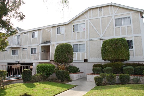 A white building with a balcony and a green bush in front.
