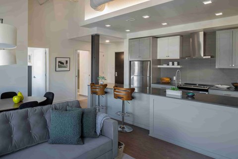 A modern kitchen with a grey couch and bar stools.