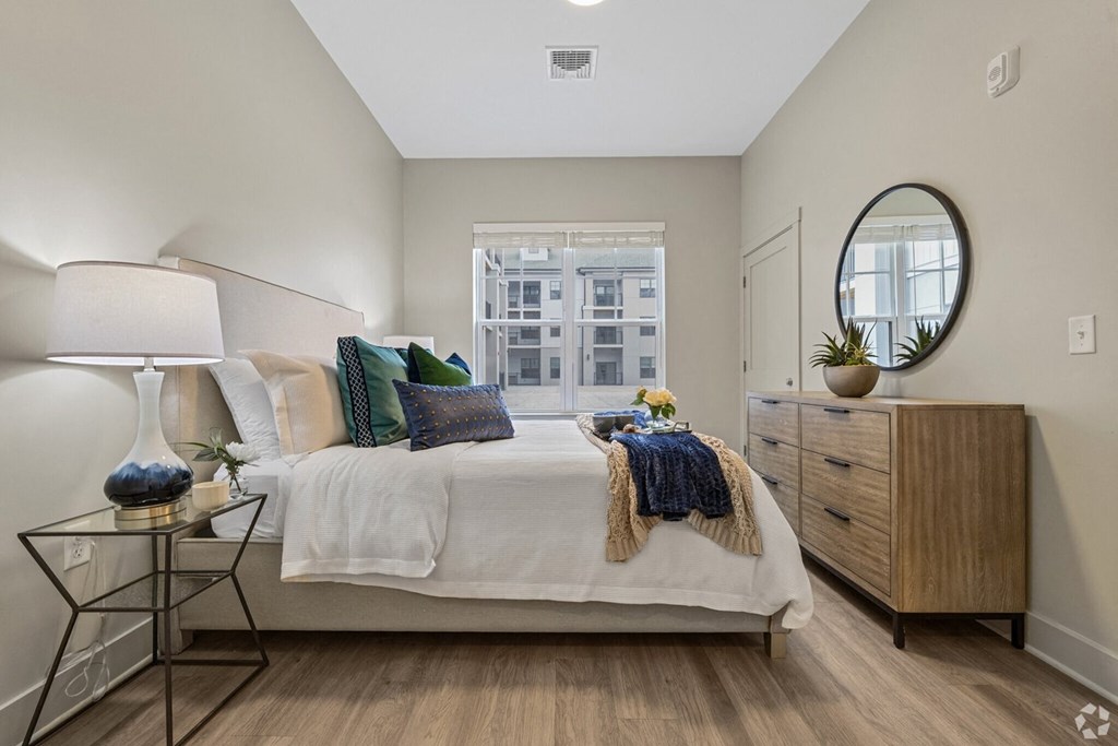 A bedroom with a bed, nightstand, and a window with a view of a city.