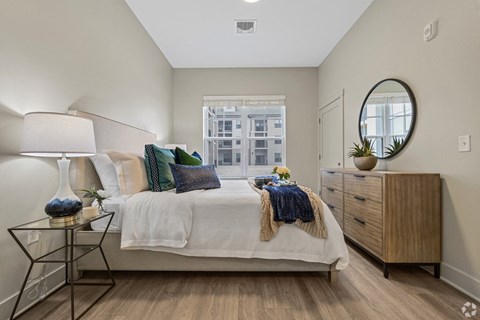 A bedroom with a bed, nightstand, and a window with a view of a city.