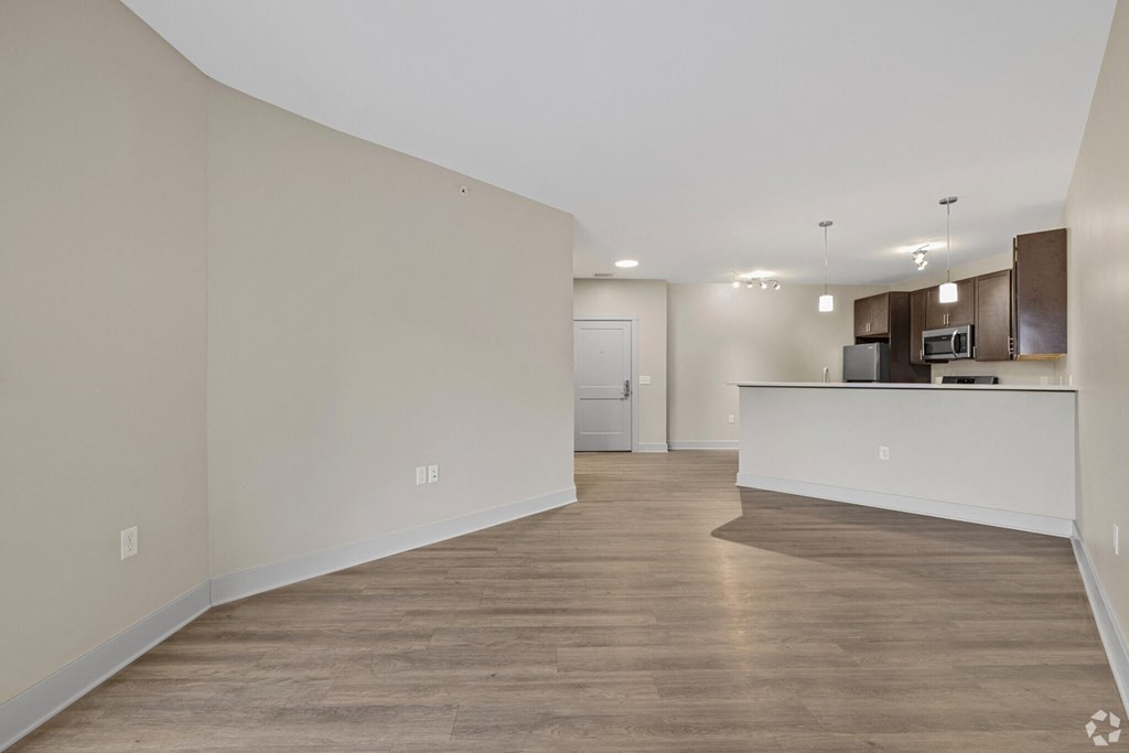 A spacious room with wooden flooring and a kitchen area in the background.