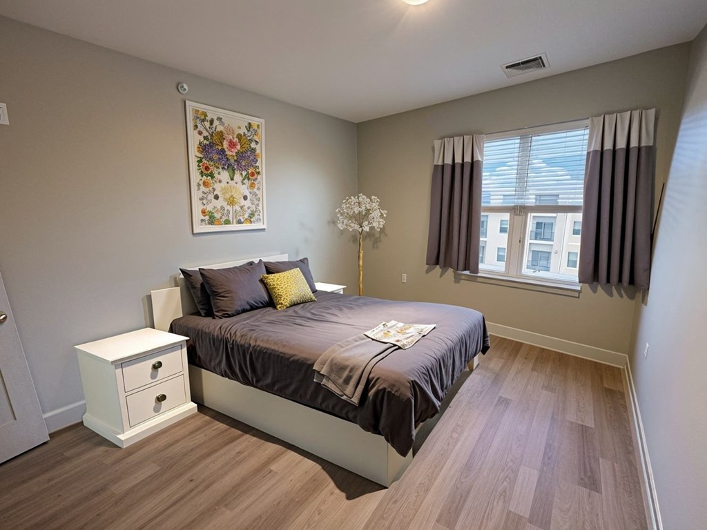 A bedroom with a bed, nightstand, and a painting on the wall.