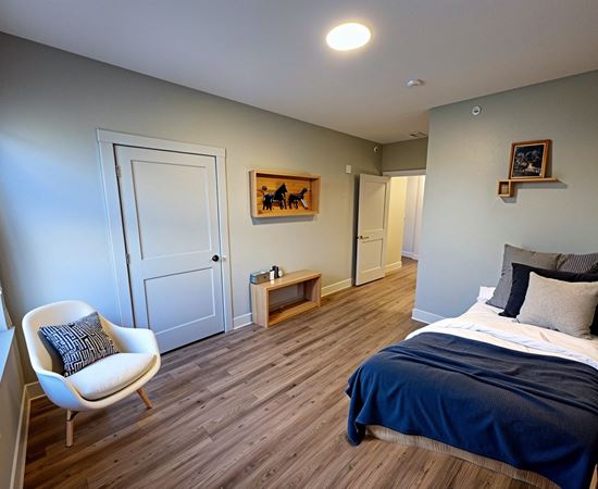 A bedroom with a bed, chair, and artwork.