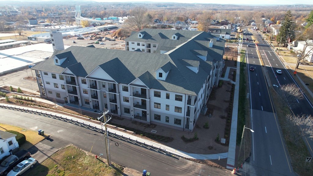 A large white building with a grey roof is surrounded by roads.