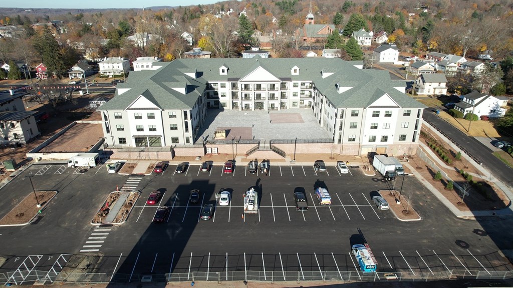 A large white building with a green roof is surrounded by a parking lot.