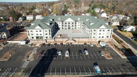 A large white building with a green roof is surrounded by a parking lot.