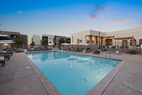 A large swimming pool is surrounded by lounge chairs and umbrellas.