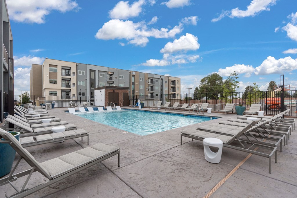 A pool area with sun loungers and apartment buildings in the background.