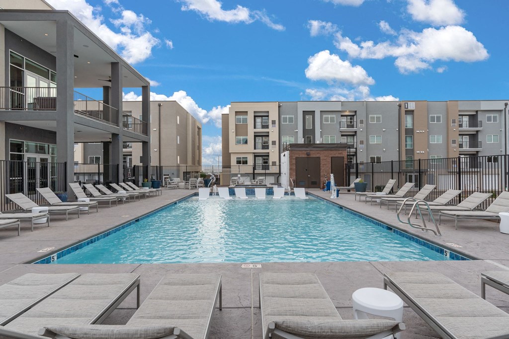 A swimming pool surrounded by lounge chairs in front of apartment buildings.