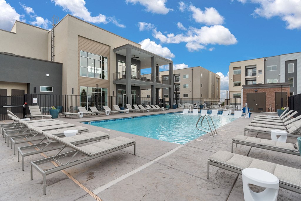A pool area with sun loungers and a building in the background.
