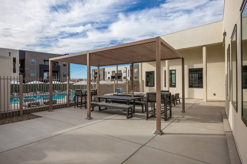 A patio with a table and chairs is surrounded by a pool and buildings.