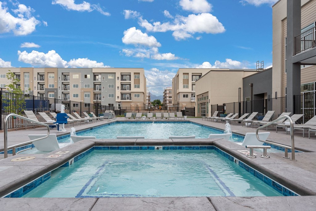 A large outdoor swimming pool with lounge chairs and apartment buildings in the background.