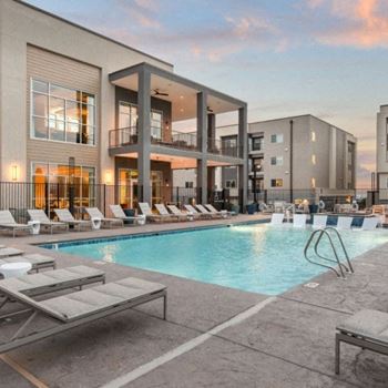 A modern building with a pool and lounge chairs.