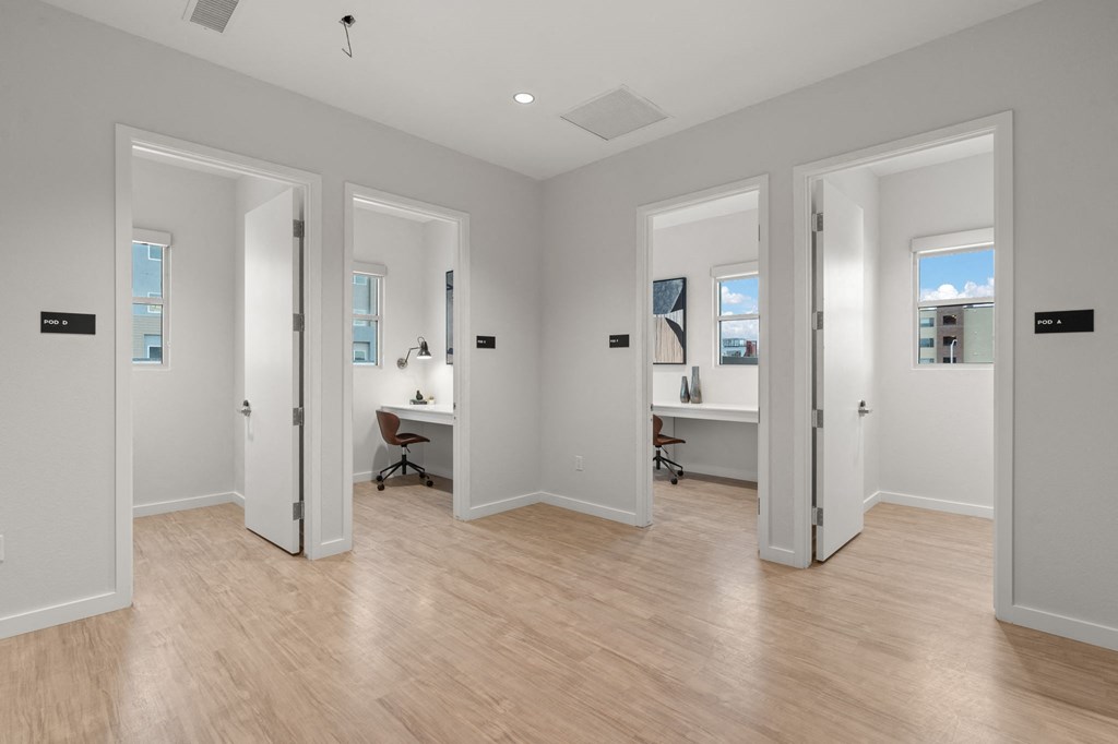 A room with white walls and wooden flooring with four doors.