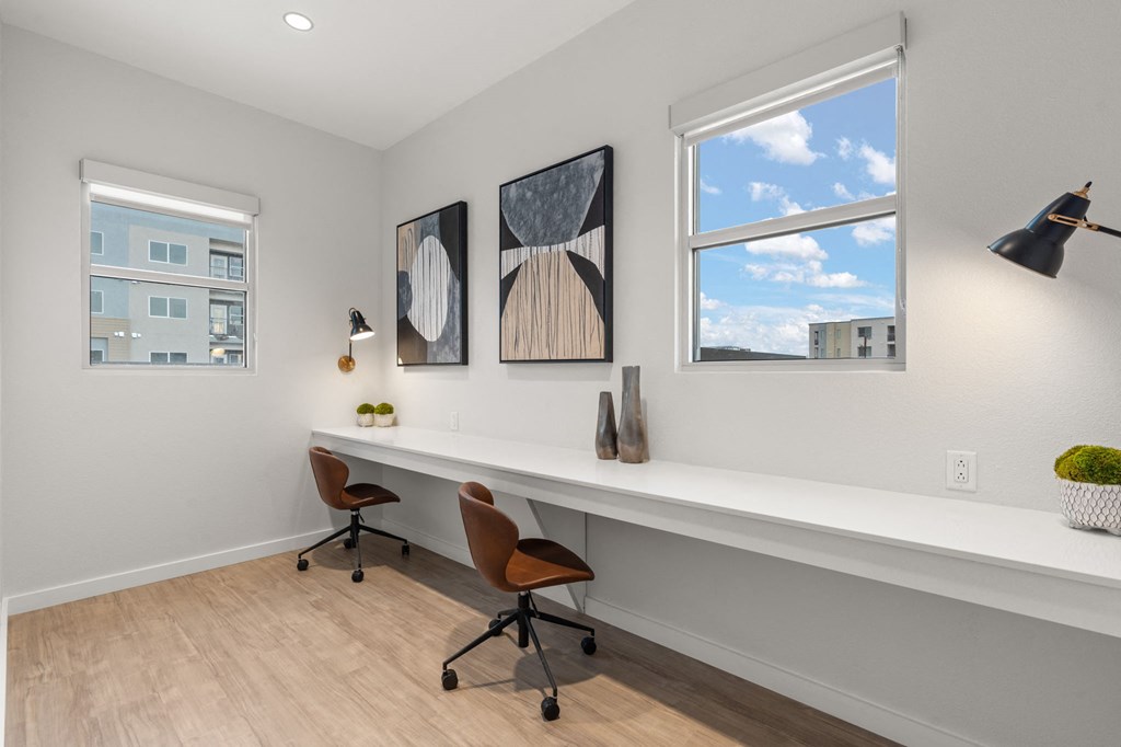 A room with a desk, chairs and two paintings on the wall.