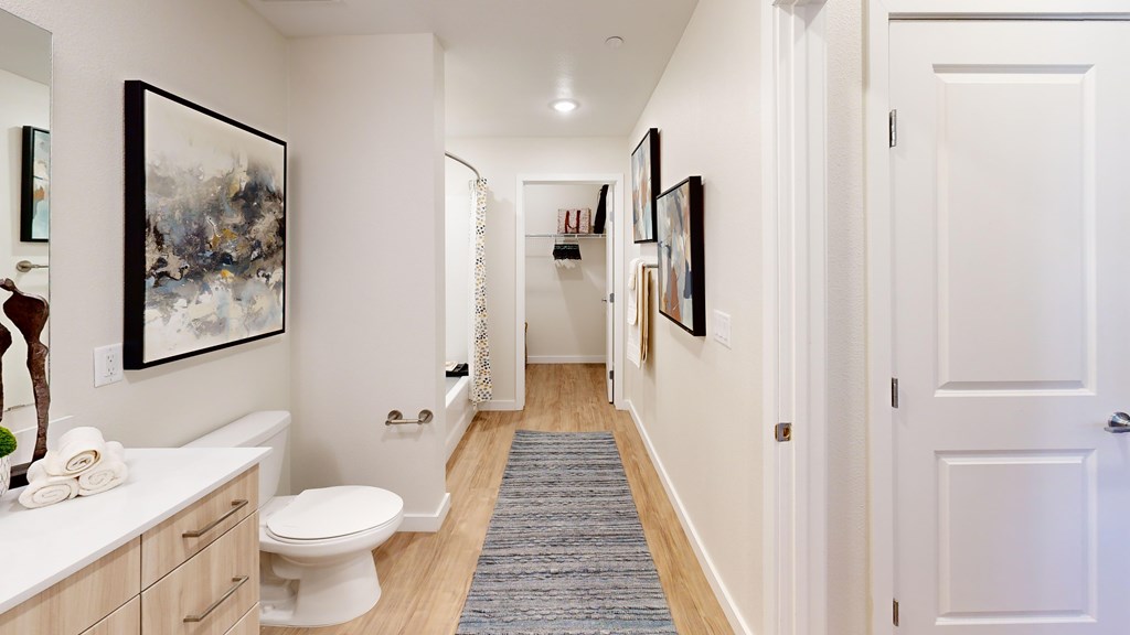 A hallway with a toilet, sink, and pictures on the wall.