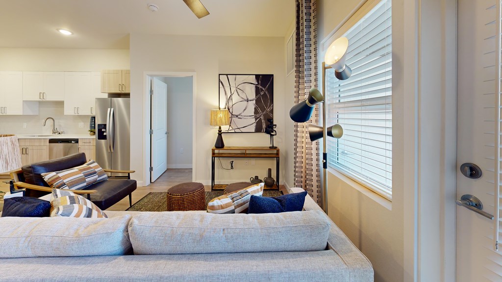A modern living room with a grey sofa and a kitchen area in the background.