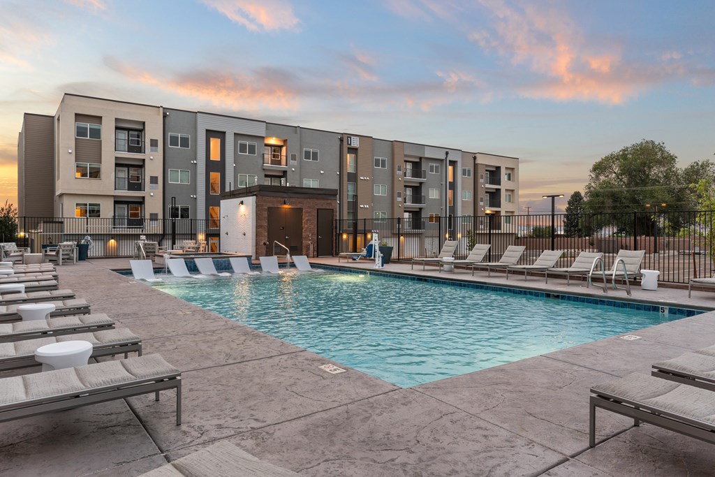 A swimming pool surrounded by lounge chairs in front of apartment buildings.