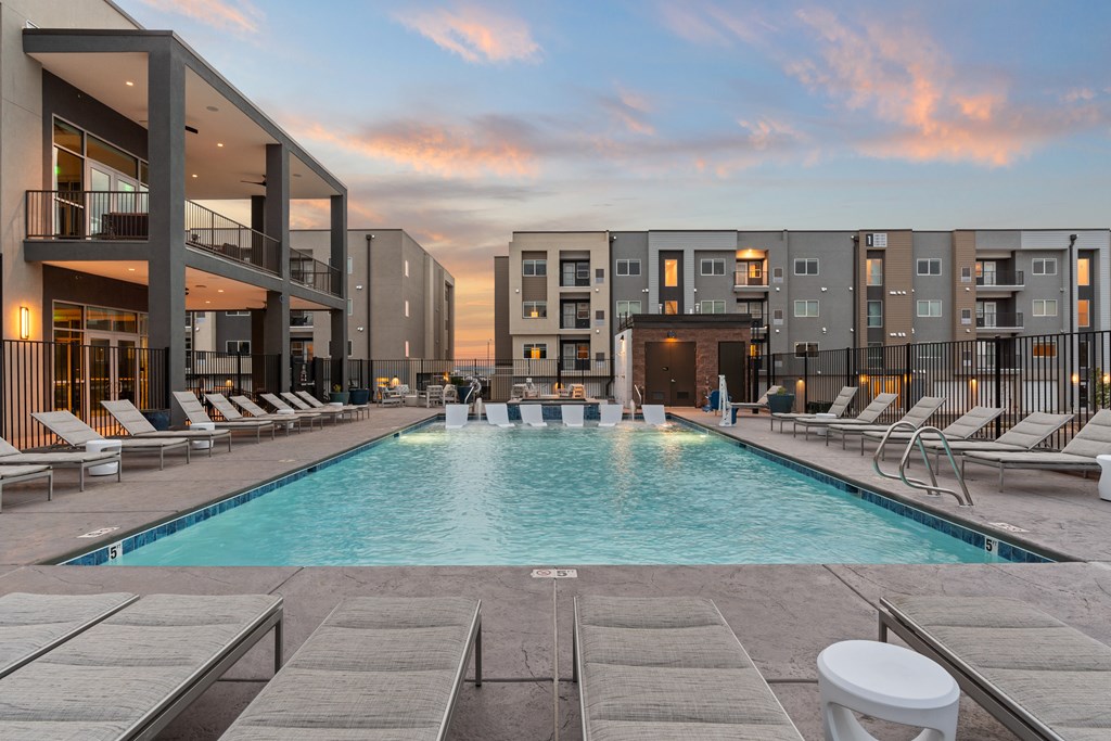 A swimming pool surrounded by lounge chairs and buildings in the background.
