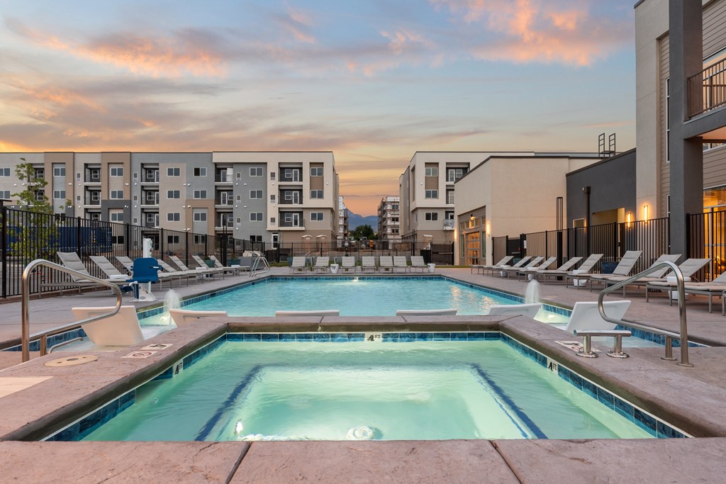 A swimming pool surrounded by lounge chairs in front of apartment buildings.