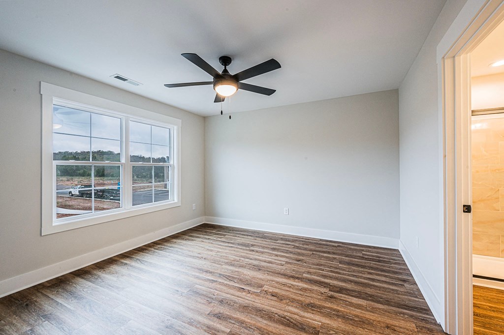 A room with a ceiling fan and a window overlooking a parking lot.