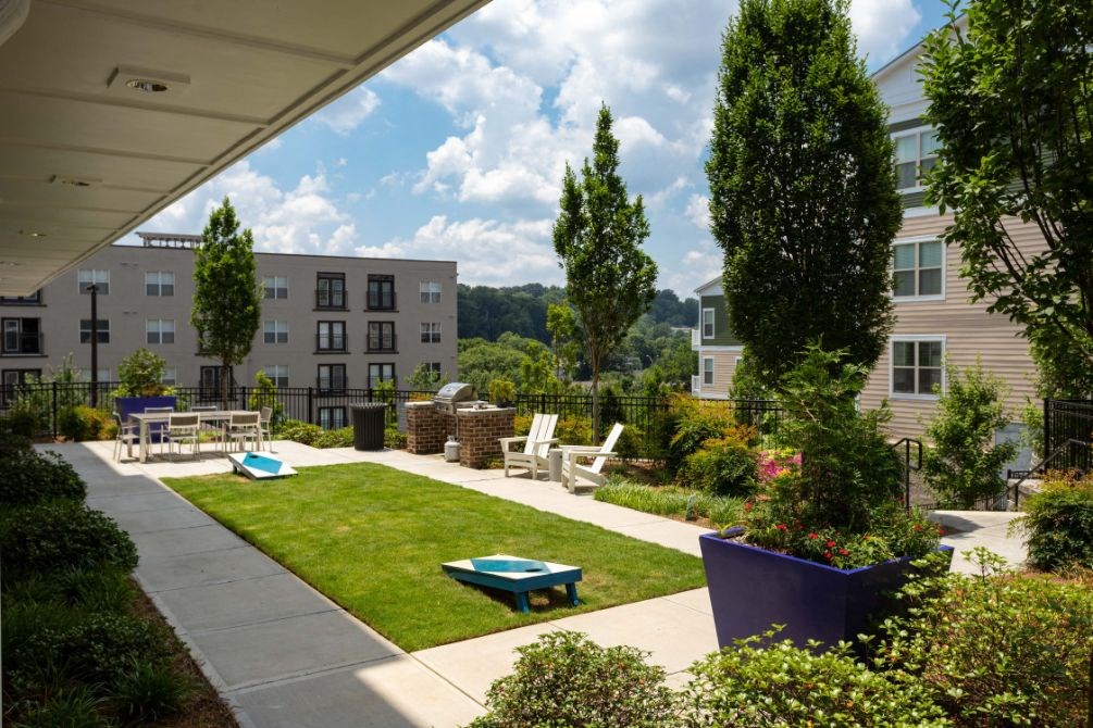 a grassy area with a picnic table and lounge chairs in front of an apartment building