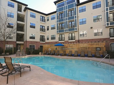 an outdoor pool with lounge chairs and a blue umbrella in front of an apartment building