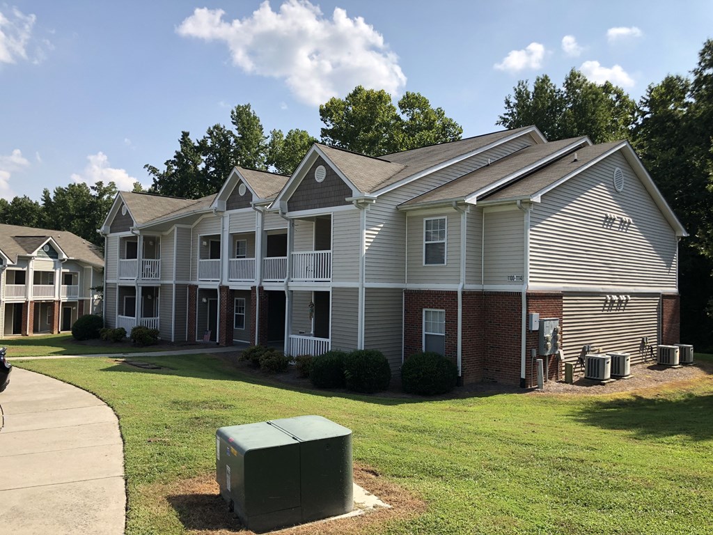an apartment building with a green lawn and a trash can