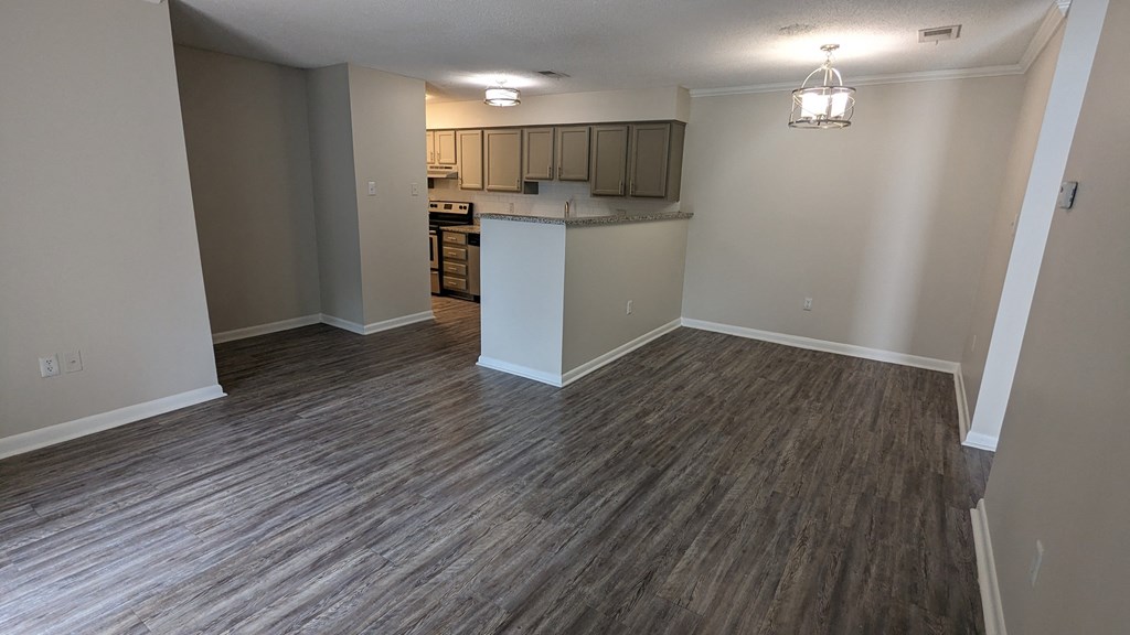 an empty living room with a kitchen in the background