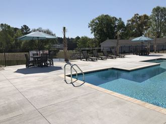a swimming pool and patio with chairs and umbrellas