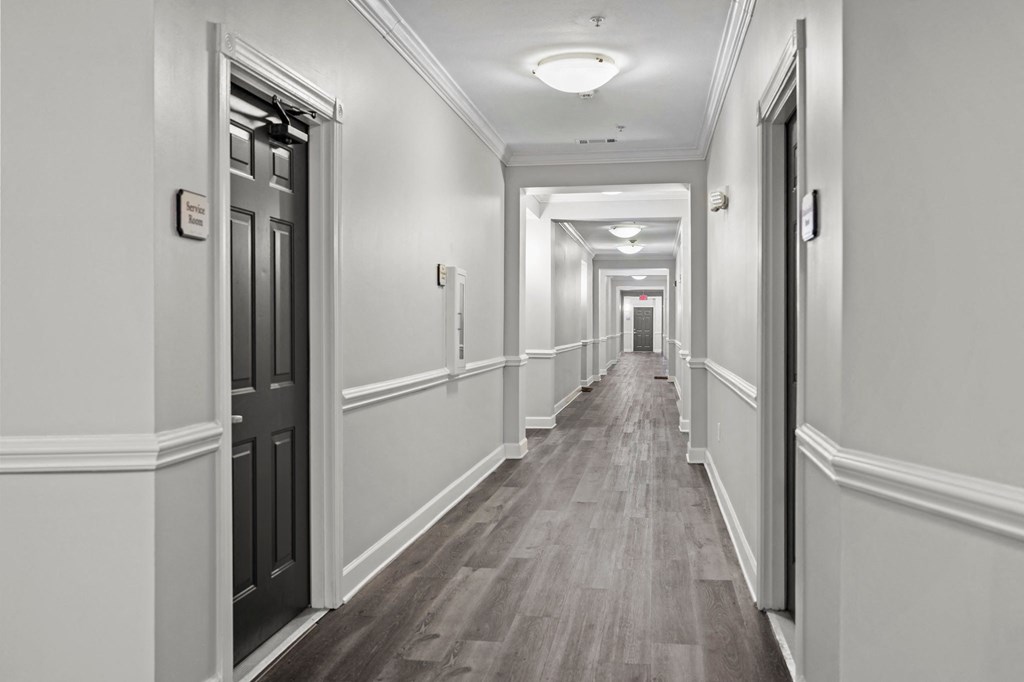 a corridor in a building with white walls and wooden floors and black doors