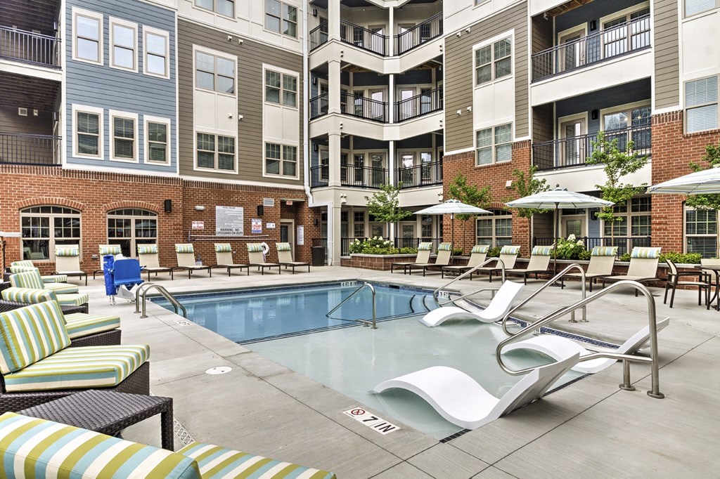 a swimming pool with chairs and umbrellas in front of an apartment building