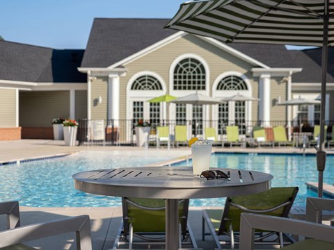A table with a glass of milkshake and sunglasses on it in front of a pool.