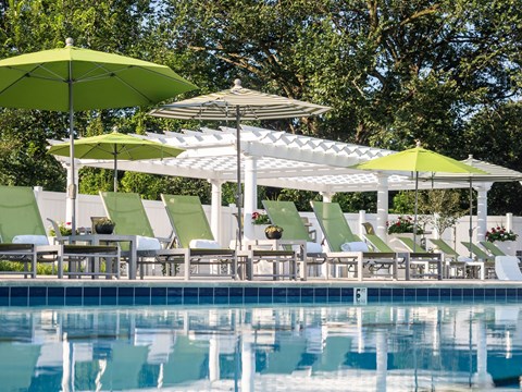 A poolside area with green umbrellas and white chairs.