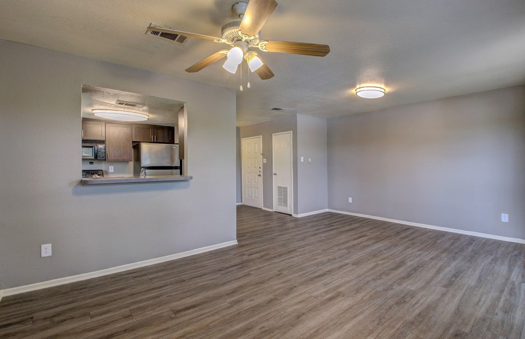 an empty living room with a ceiling fan and a kitchen