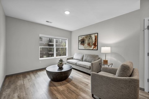 A living room with a grey couch, a grey armchair, a coffee table, and a painting on the wall.