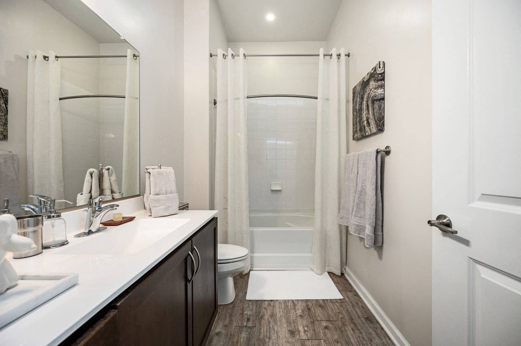 A bathroom with a white sink, a toilet, a shower with a white curtain, and a wooden floor.