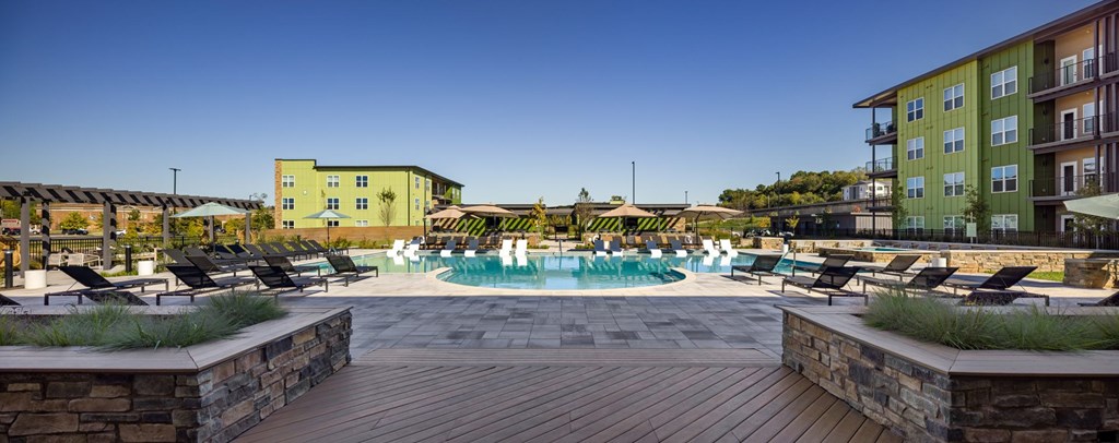 A pool area with a wooden deck and a building in the background.