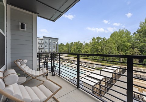 A balcony with a chair and table overlooking a pool and trees.