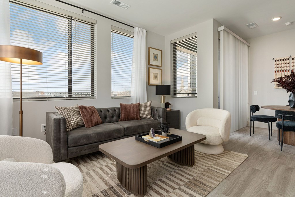 A modern living room with a grey couch, a white chair, a brown coffee table, and a large window with white curtains.