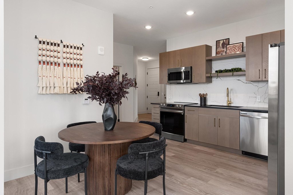 A kitchen with a round table and chairs and a vase of flowers on it.