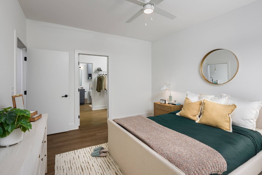 A bedroom with a bed, a dresser, a mirror, and a ceiling fan.