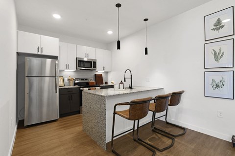 A kitchen with a refrigerator, microwave, and a counter with chairs.
