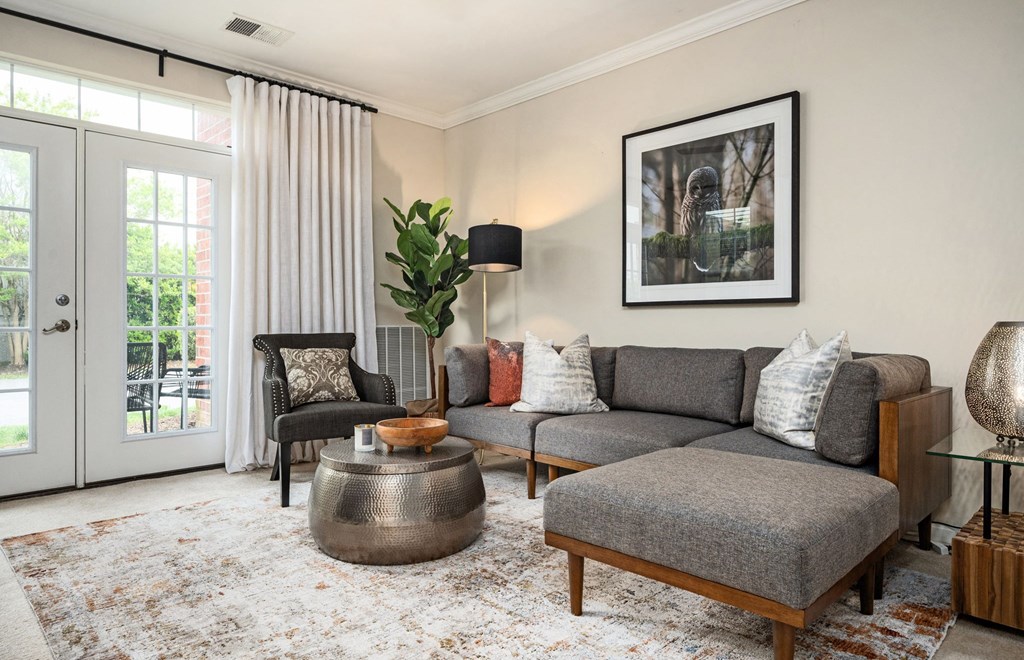 A living room with a grey couch, a coffee table, and a large window with curtains.