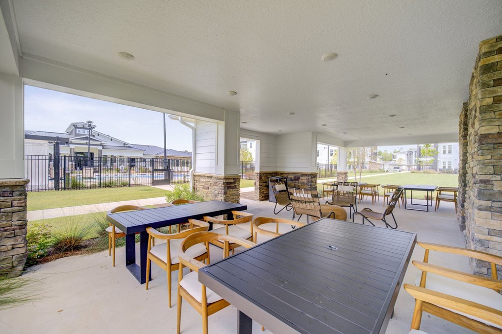 A modern outdoor dining area with a stone pillar and a view of a fenced area with a building in the distance.