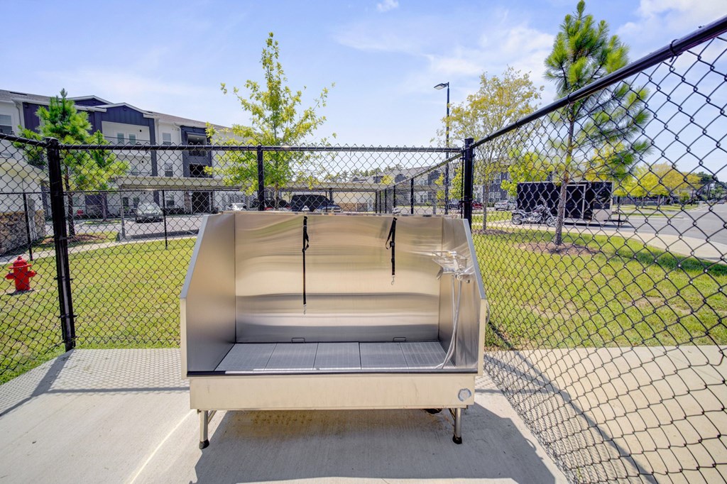 A large, empty, beige-colored hot tub sits on a concrete slab in front of a chain-link fence.