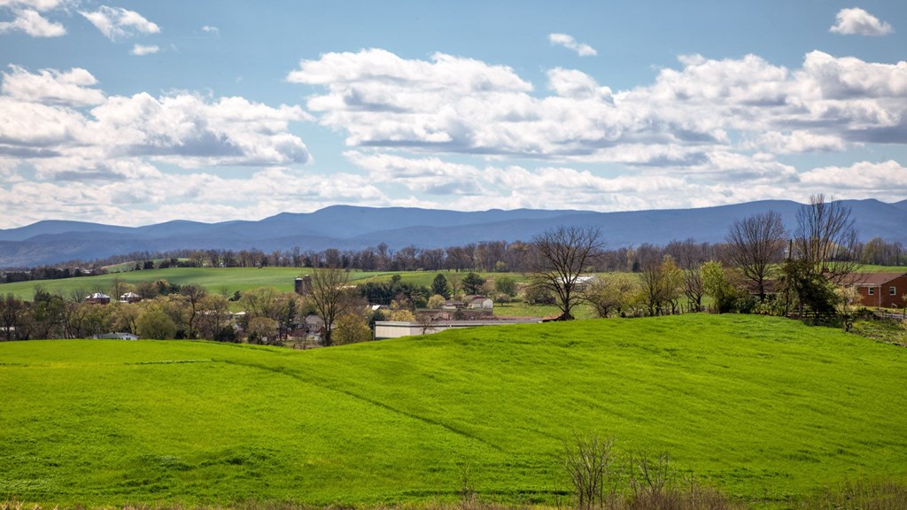 A green field with trees and mountains in the distance under a blue sky with clouds at The Mark Townhomes Apartments, Harrisonburg, VA